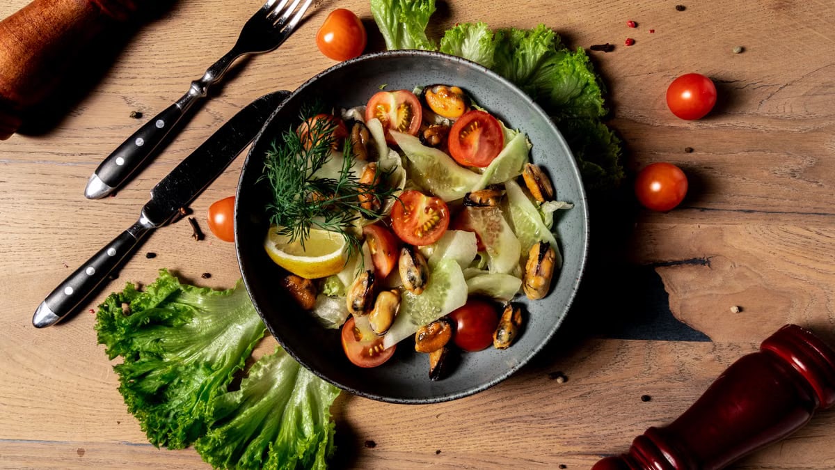 A vibrant salad featuring cherry tomatoes, mussels, and fresh lettuce with a lemon garnish. Perfect for a healthy meal.